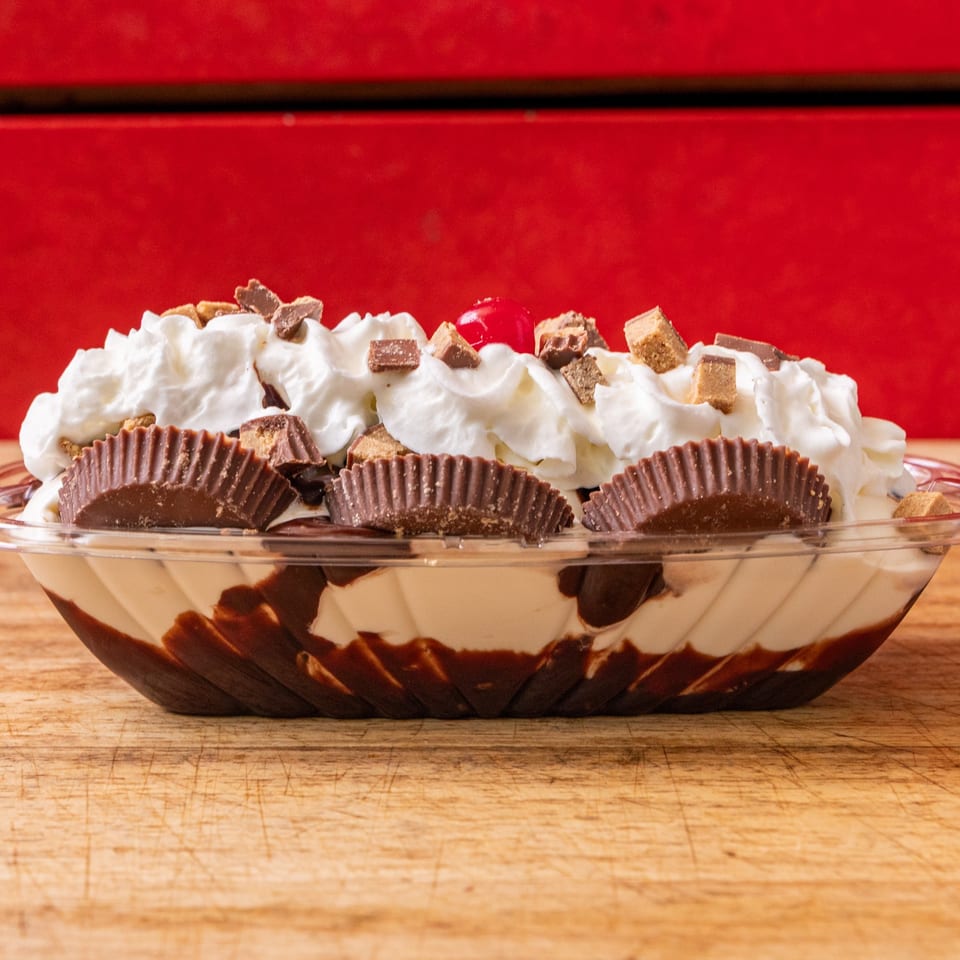 A banana split with whipped cream, chocolate syrup, peanut butter cups, and a cherry on top.