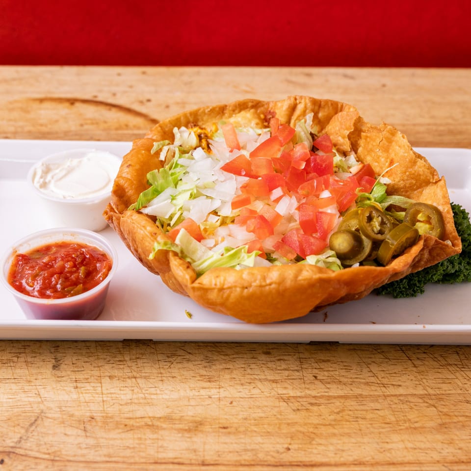 A taco salad in a crispy fried shell with lettuce, tomatoes, onions, and jalapeños, with salsa and sour cream.