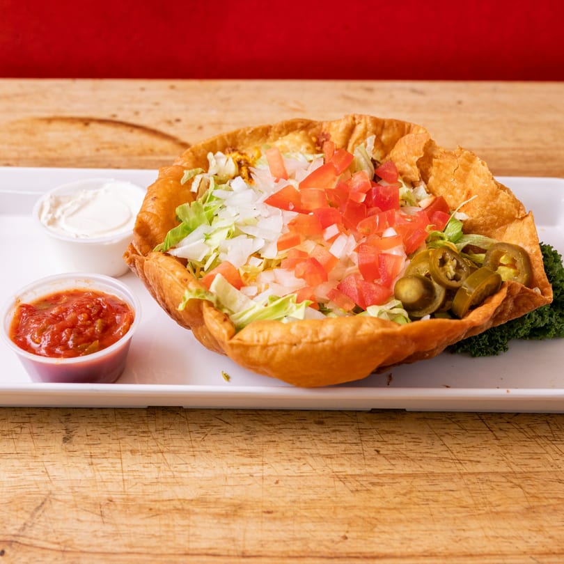 A taco salad in a crispy fried shell with lettuce, tomatoes, onions, and jalapeños, with salsa and sour cream.