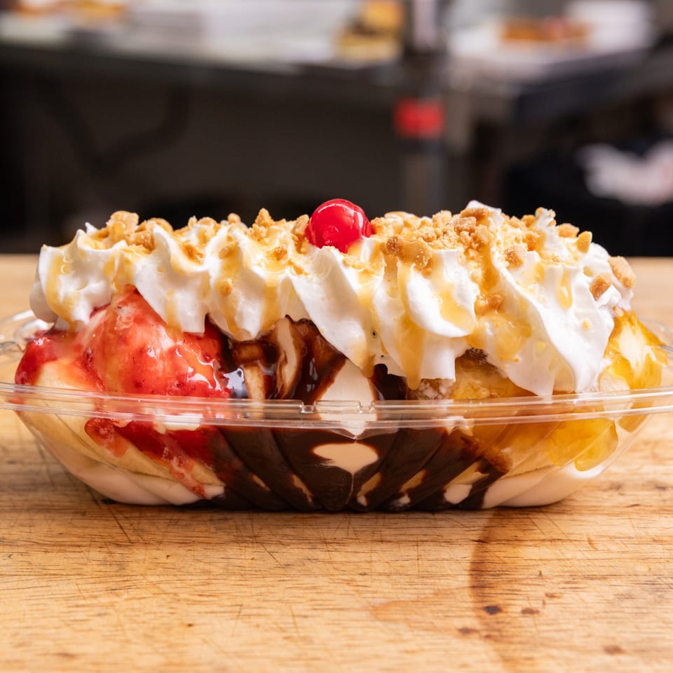A banana split with whipped cream, caramel, nuts, and a cherry on a wooden table.