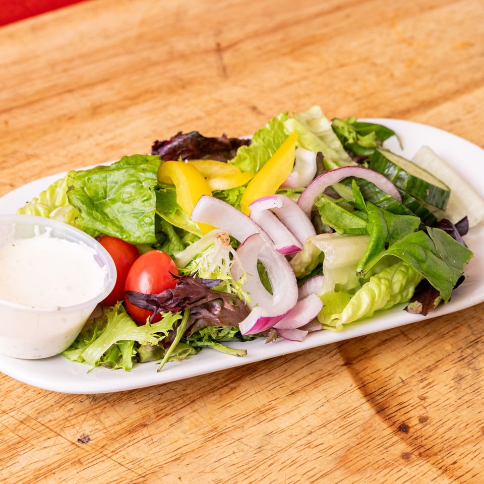 A fresh garden salad with lettuce, tomatoes, cucumbers, red onions, and bell peppers, with dressing.