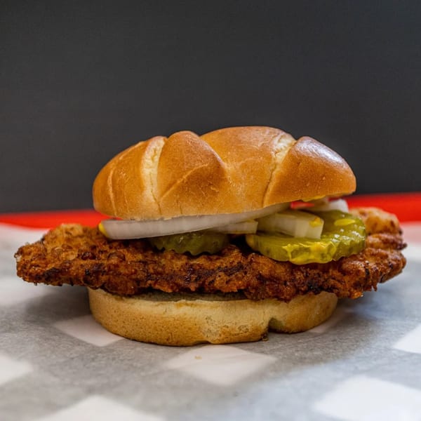 Our Place's crispy fried chicken sandwich with pickles and onions on a bun.