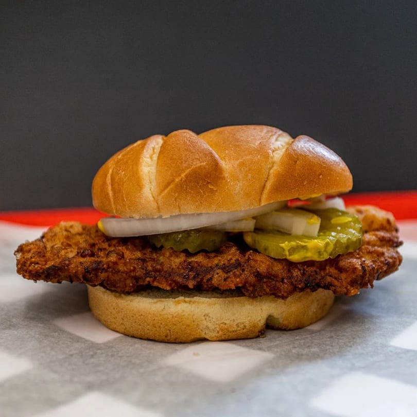 Our Place's crispy fried chicken sandwich with pickles and onions on a bun.