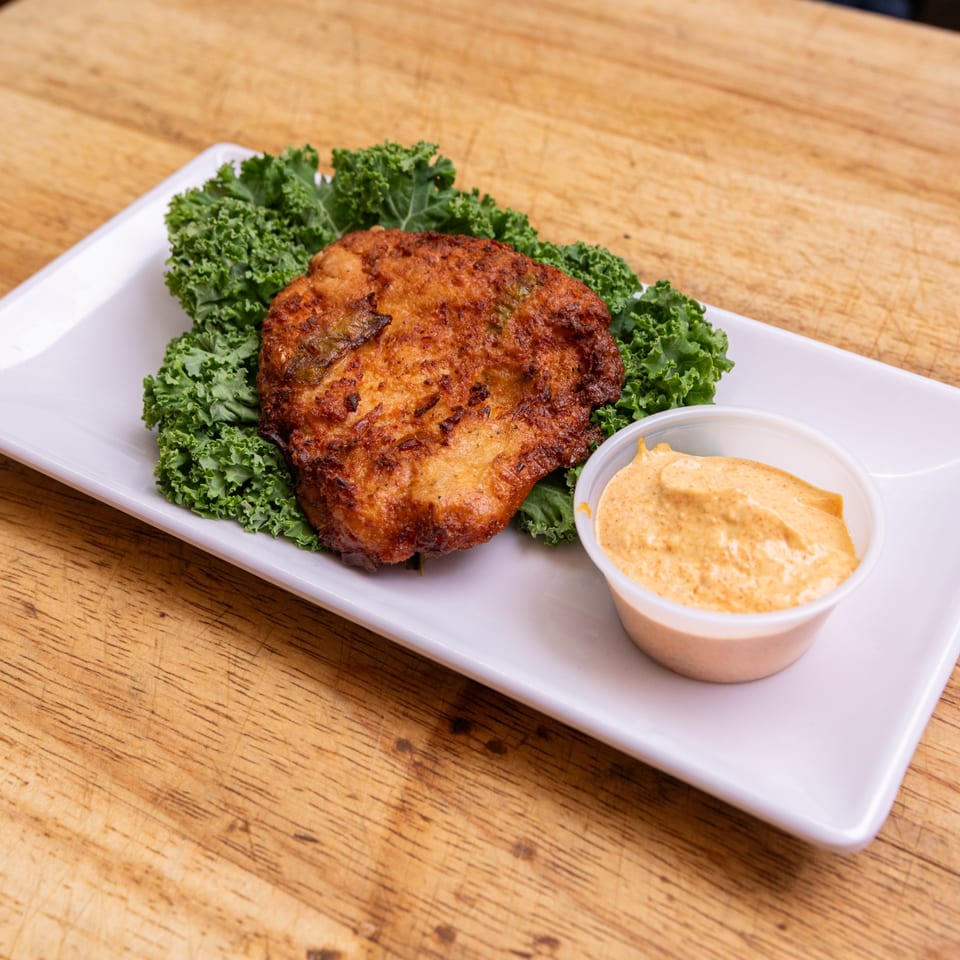 Our Place's golden-brown fried fritter, served on kale with a side of creamy orange sauce.