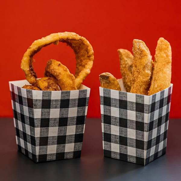 Two checkered containers, one with onion rings and the other with potato wedges, against a red background.