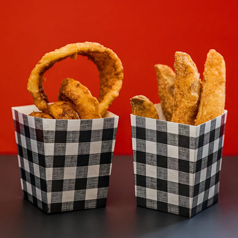 Two checkered containers, one with onion rings and the other with potato wedges, against a red background.