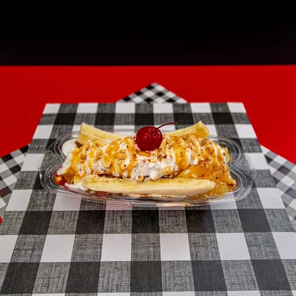Our Place banana split with whipped cream, nuts, caramel, and a cherry on a checkered tablecloth.